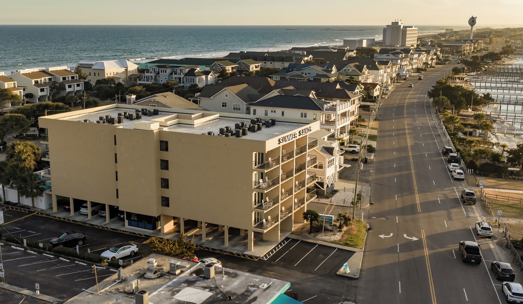 A multi-story hotel with a rooftop pool, located near a coastal road with a view of the ocean.