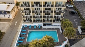 Um hotel com vários andares e área de piscina no terraço, incluindo espreguiçadeiras e uma piscina.