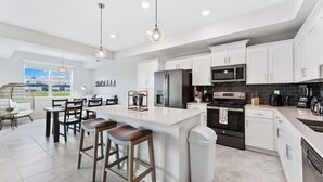 A modern kitchen with white cabinets, a large island with bar stools, stainless steel appliances, and a view of the outdoors.
