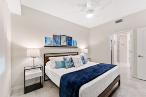 Un dormitorio con cama, mesitas de noche, ventilador de techo y una obra de arte en la pared.