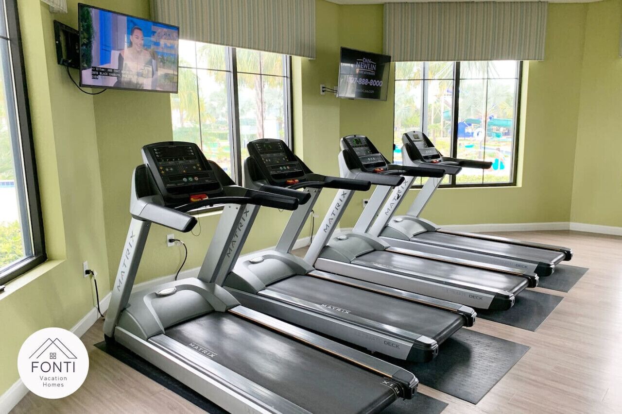 Une salle de sport équipée de tapis de course, d’un téléviseur et de grandes fenêtres.