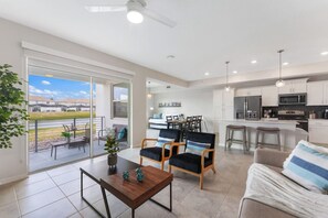 Eine moderne Küche mit weißen Schränken, einer Mikrowelle und einem Kühlschrank. Es gibt einen Essbereich mit Tisch und Stühlen, sowie ein Balkon mit Blick auf die Landschaft.