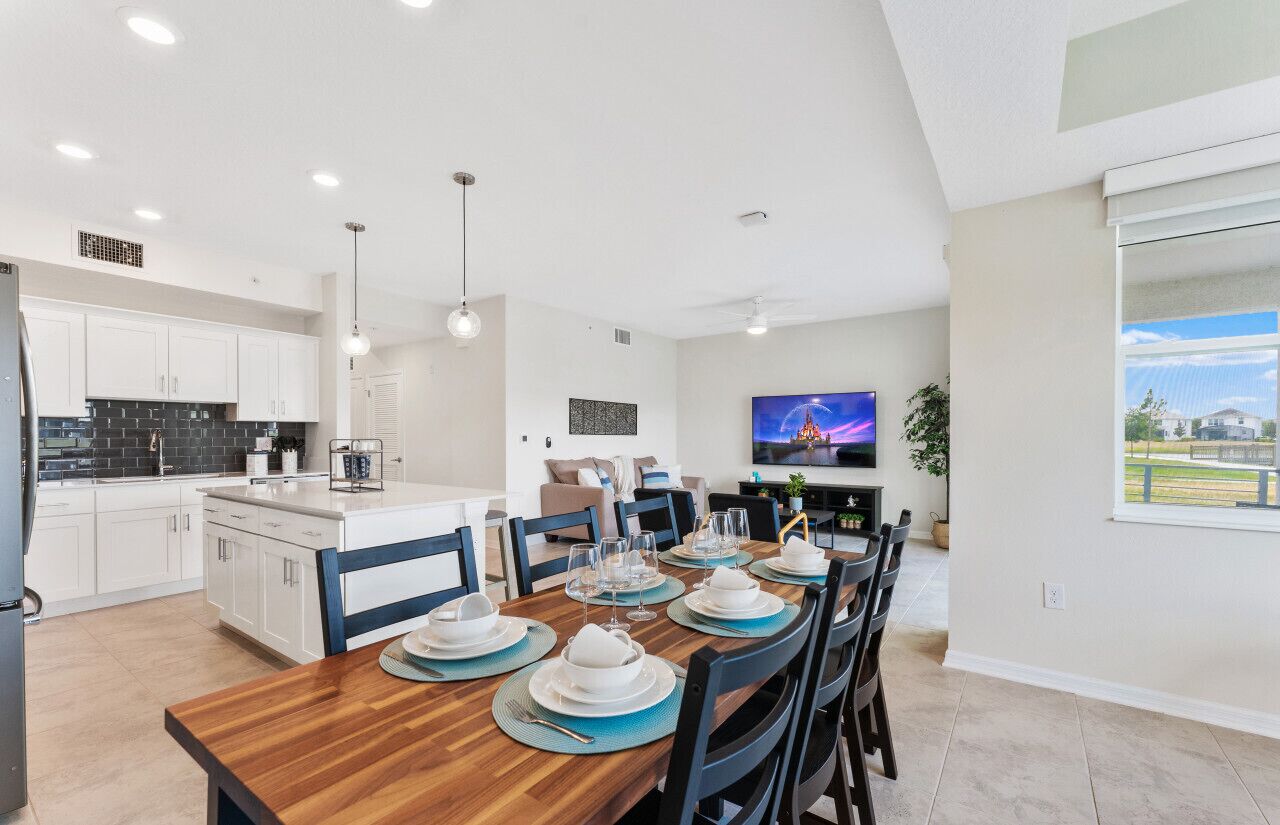 A modern kitchen with white cabinets, a black backsplash, and a dining area set for six with a wooden table and black chairs.