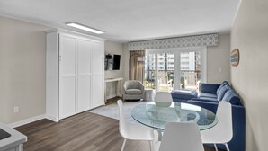 Un salon moderne avec une table à manger en verre, des chaises blanches, un canapé bleu et un fauteuil gris.