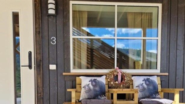 Eine Holzbank mit Kissen, eine Tür und ein Fenster mit Blick auf ein Haus.