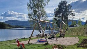 Ein Spielplatz mit Schaukel, Wippe und einer Bank in der Nähe eines Sees.