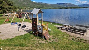 Ein Spielplatz mit Schaukeln und Klettergerüsten in der Nähe eines Sees mit Picknickplatz und Bänken.