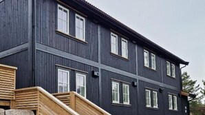 Ein zweistöckiges Gebäude mit dunkler Fassade, einer Holztreppe zum Eingang und einer Steinmauer davor.