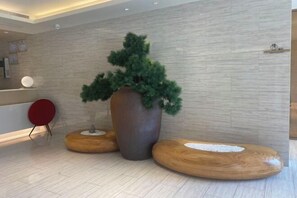 A modern lobby with a reception desk, a large potted tree, and wooden seating areas. - JI Hotel (Xiamen SM Square Chenggong Avenue) (Xiamen)