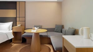 Moderni hotellihuone, jossa on sänky, pieni pyöreä pöytä, sohva ja sohvapöytä.