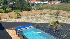 A swimming pool with a wooden deck, lounge chairs, and a view of the surrounding area.