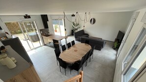 A spacious living area with a wooden dining table, black chairs, a grey sofa, and a staircase leading to an upper level.