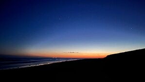 A coastal landscape at dusk with a clear sky, a silhouette of a cliff, and a calm sea.