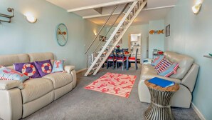 A spacious living room with a beige sofa, a patterned rug, and a staircase leading to a dining area. - 3 Bed in Kingswear (oc-a29168) (Dartmouth)