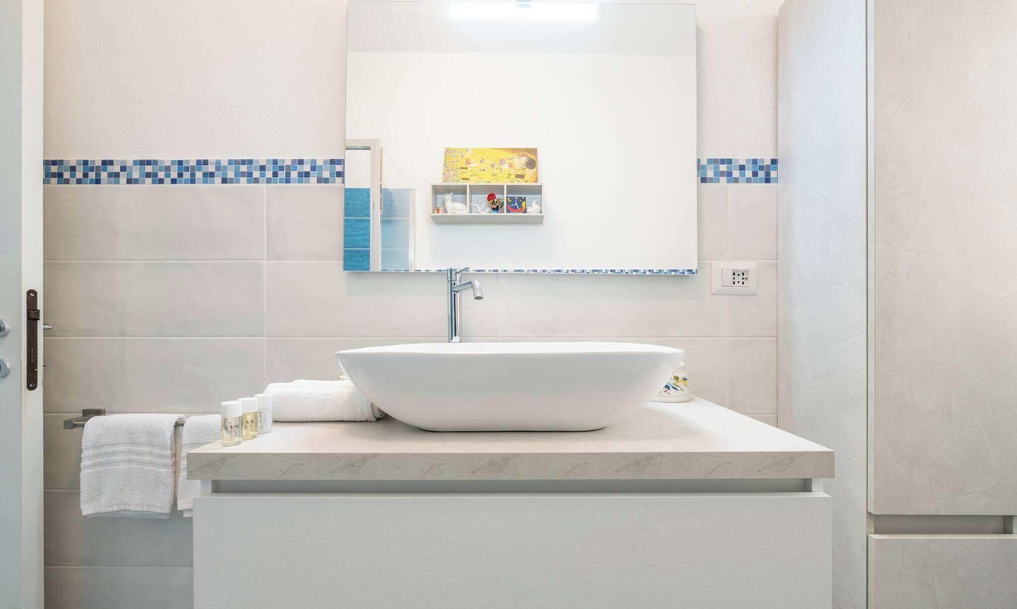 A modern bathroom with a large vessel sink, a mirror above it, and a small shelf with toiletries.