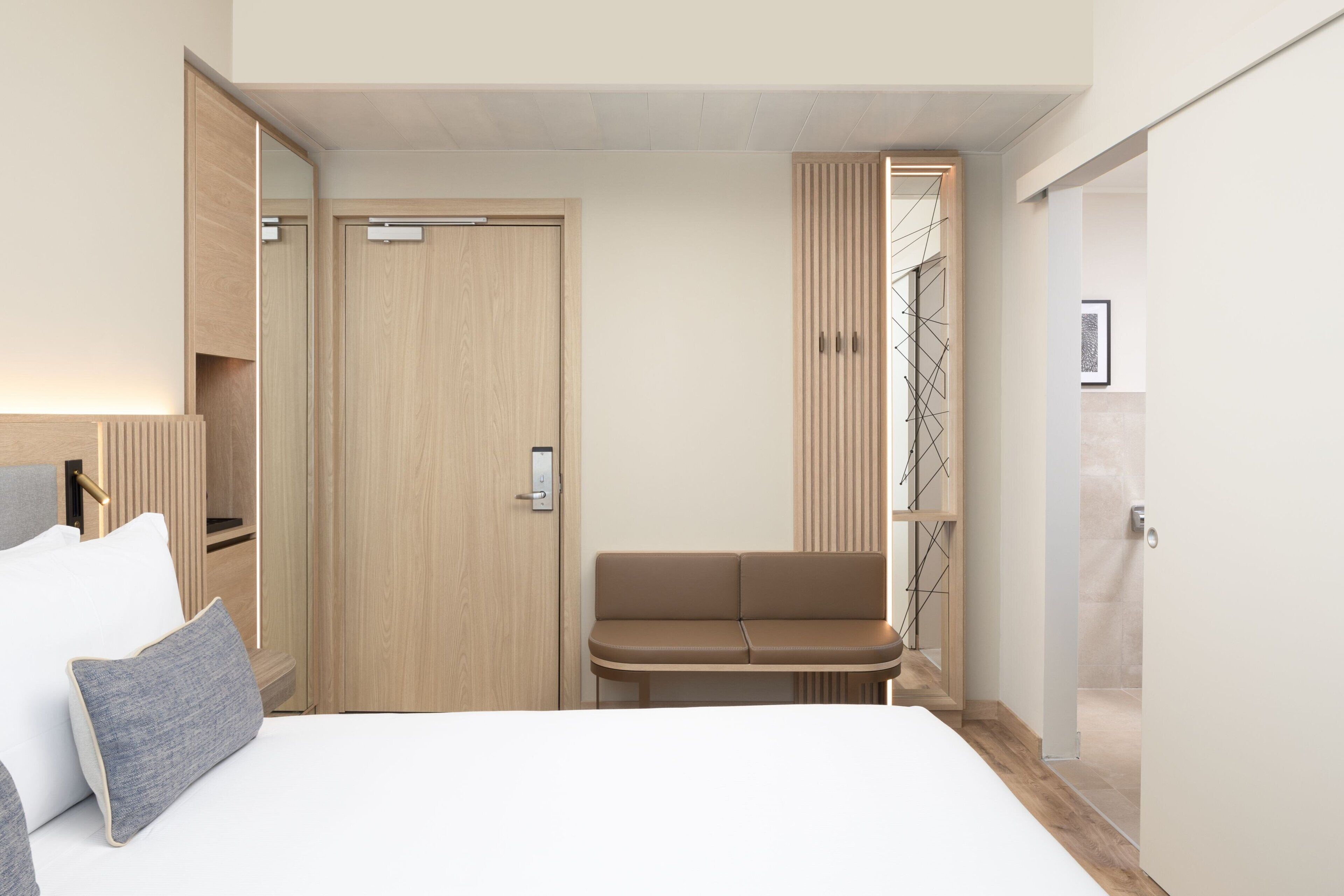 A hotel room with a bed, a bench, a wardrobe, and a door leading to a bathroom.