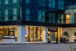 Een gevel van een Courtyard by Marriott hotel met grote glasramen, een goed verlichte ingang en potplanten.