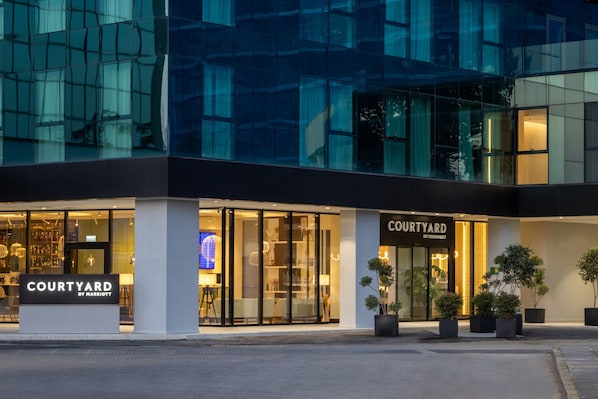 A Courtyard by Marriott hotel facade with large glass windows, a well-lit entrance, and potted plants.