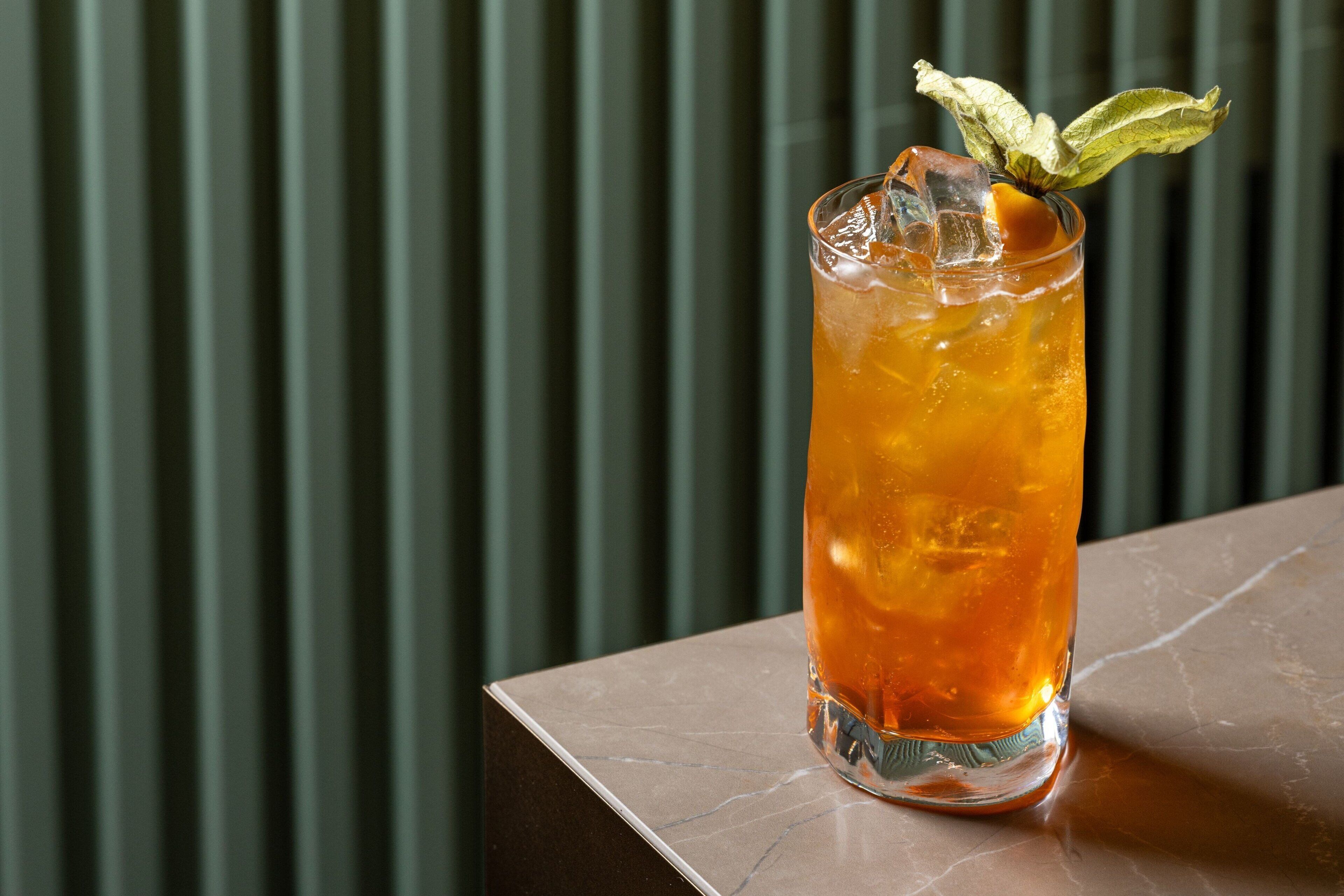 A tall glass with a beverage, ice, and a mint leaf garnish on a marble surface.