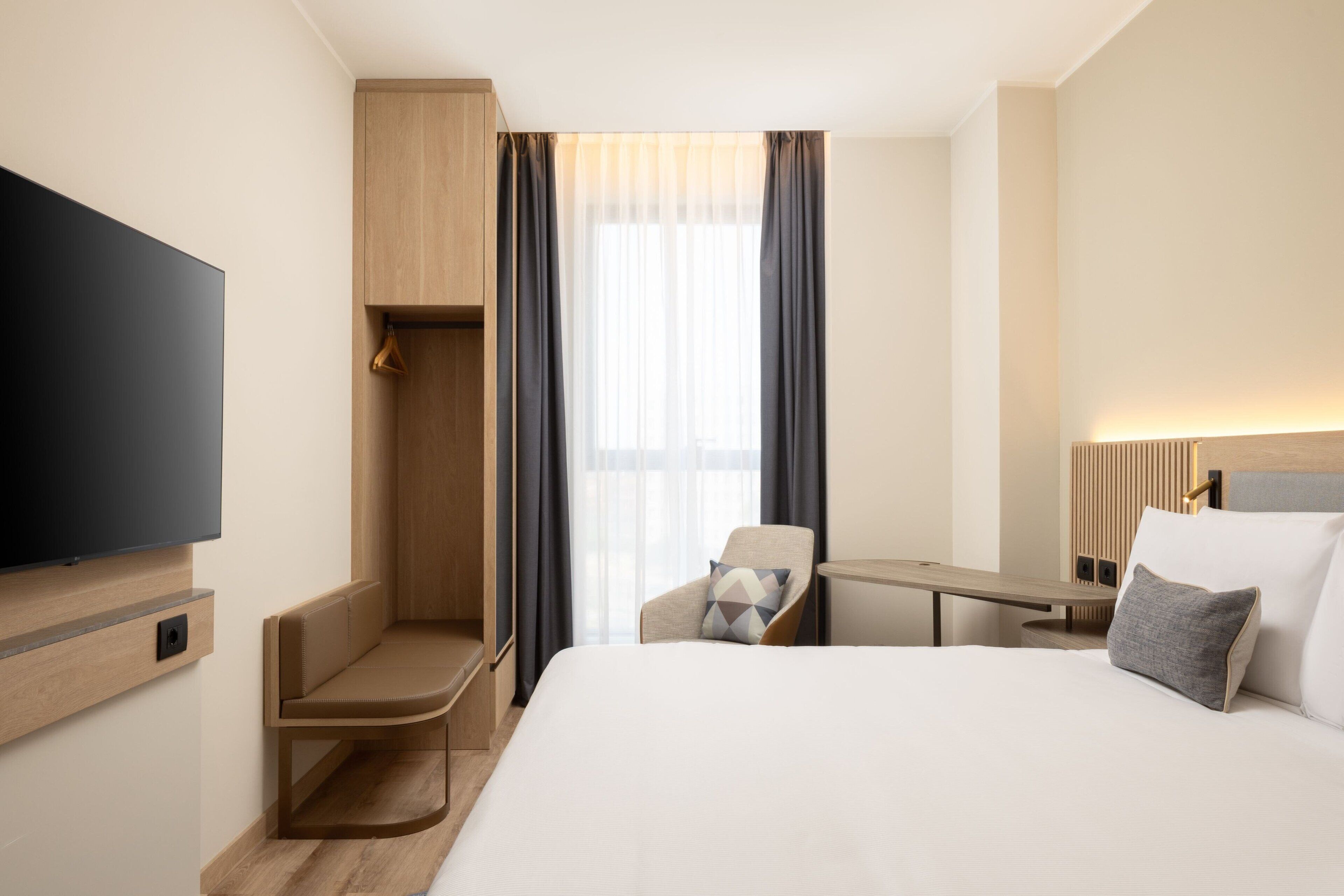 A hotel room with a bed, a TV mounted on the wall, a desk, and a chair.