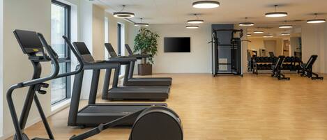 Une salle de sport équipée de plusieurs tapis de course, d’un vélo d’appartement et d’un support pour haltères.