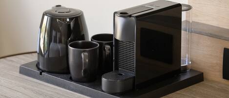 Una cocina moderna con una cafetera, dos tazas y un microondas sobre una encimera negra.