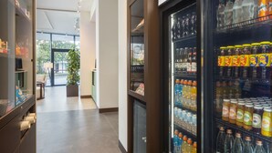 A hotel lobby with a vending machine stocked with beverages and a seating area with a potted plant. - Courtyard By Marriott Milano Linate (Milan)