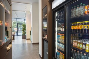 Ένας χώρος υποδοχής ξενοδοχείου με αυτόματο πωλητή γεμάτο με ποτά και μια περιοχή με καθίσματα, όπου υπάρχει και ένα φυτό σε γλάστρα.