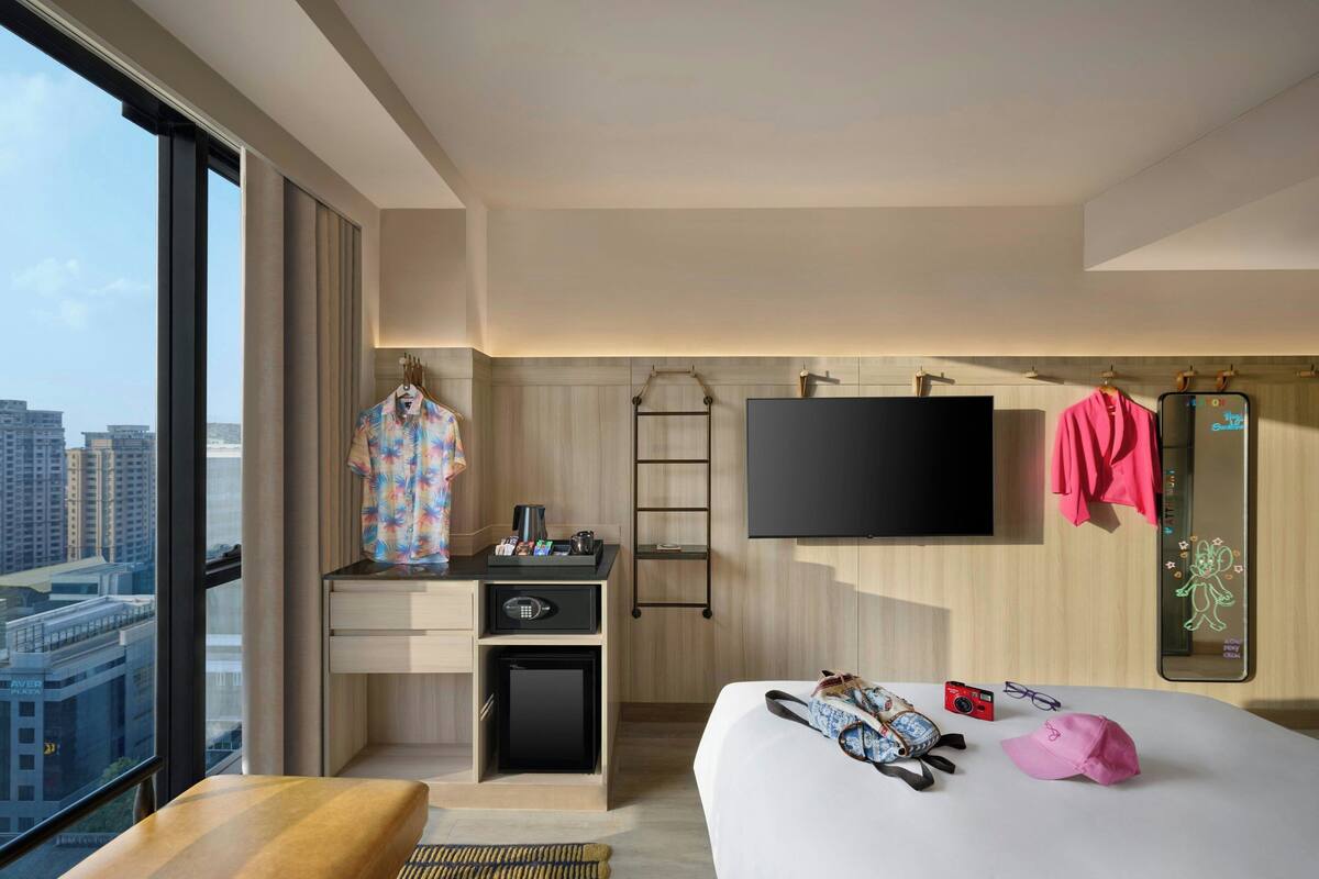 Ett modernt hotellrum med en stor säng, ett skrivbord med en dator, en TV och utsikt över staden.