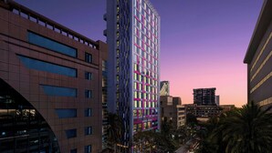 Un hotel moderno de altura con varios pisos, grandes ventanales y una fachada distintiva en rosa y azul.