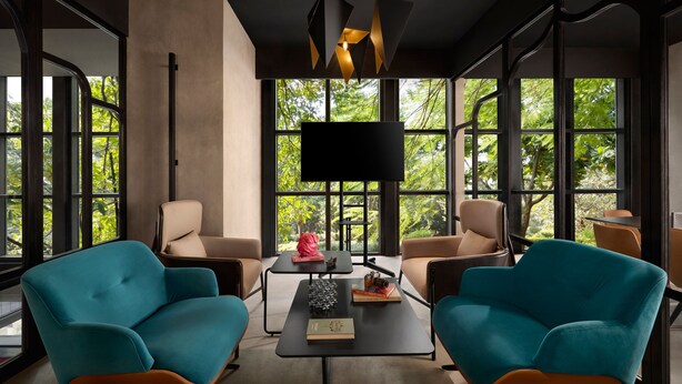 Una habitación moderna con dos sillas color turquesa, una mesa negra y un ventanal con vistas a árboles.