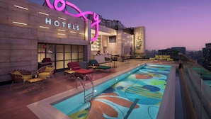 Zona de piscina en la azotea con mobiliario de relax y un letrero de neón para un hotel.
