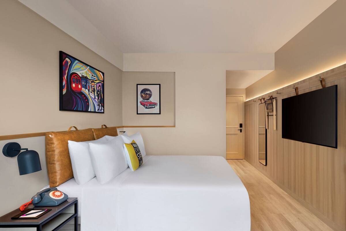 Ett modernt hotellrum med en stor säng, en platt-TV som är monterad på väggen, en tavla ovanför sängen och en väggpanel i trä.