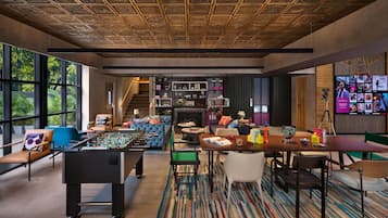 Una sala de estar moderna con una mesa de futbolín, asientos cómodos, una chimenea y una gran pantalla de televisión mostrando diversos contenidos.