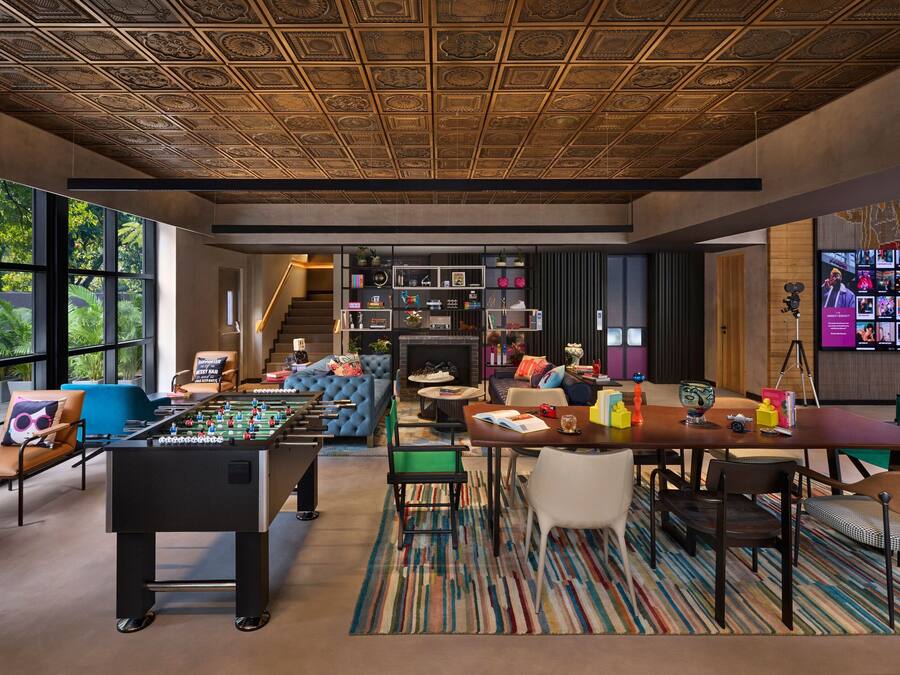 Una sala de estar moderna con una mesa de futbolín, asientos cómodos, una chimenea y una gran pantalla de televisión mostrando diversos contenidos.