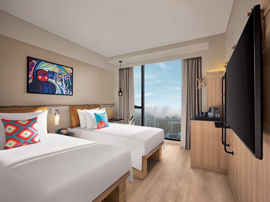 Habitación de hotel con dos camas, un televisor grande, un cuadro y vistas a la ciudad.