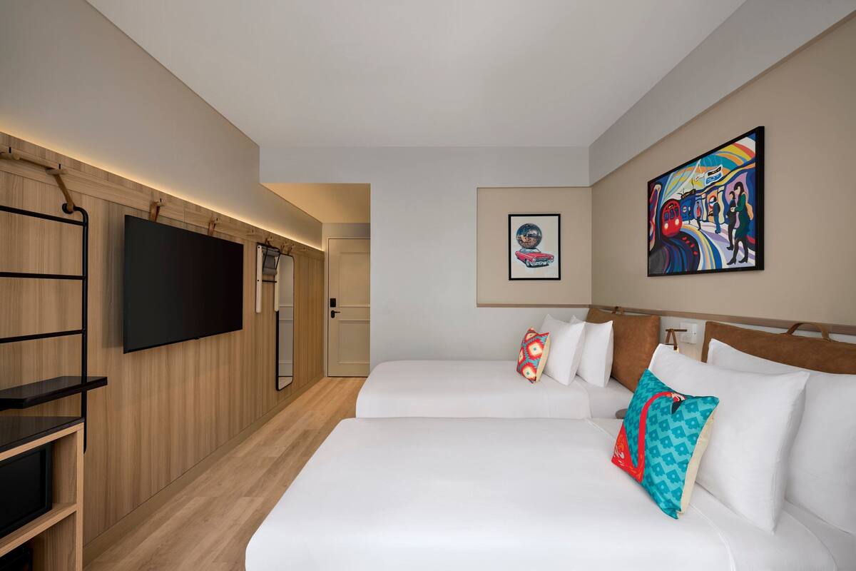 Ett hotellrum med två sängar, en tv som är monterad på väggen och konstverk på väggarna.