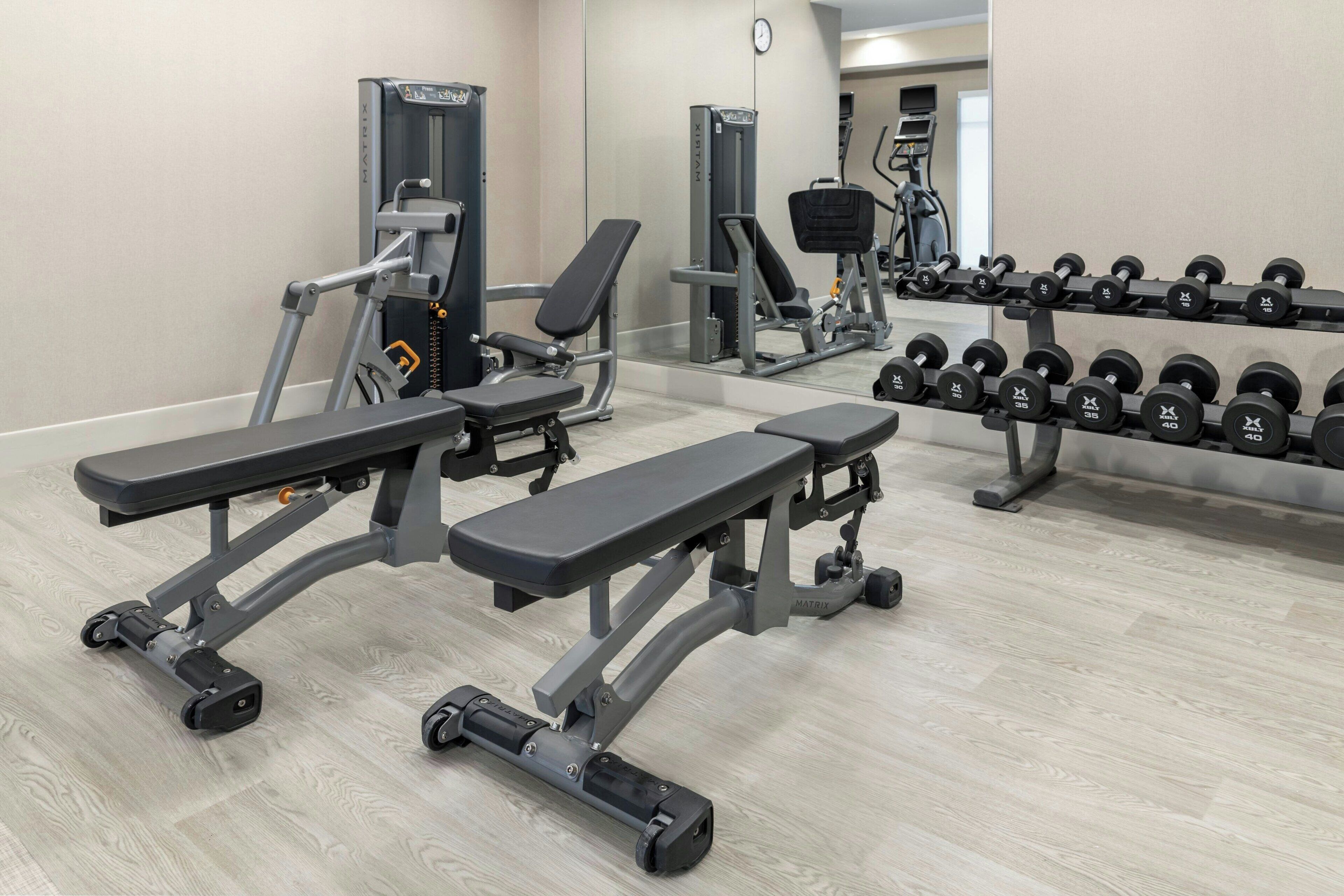 A gym with weight benches, a squat rack, and a rack of dumbbells.