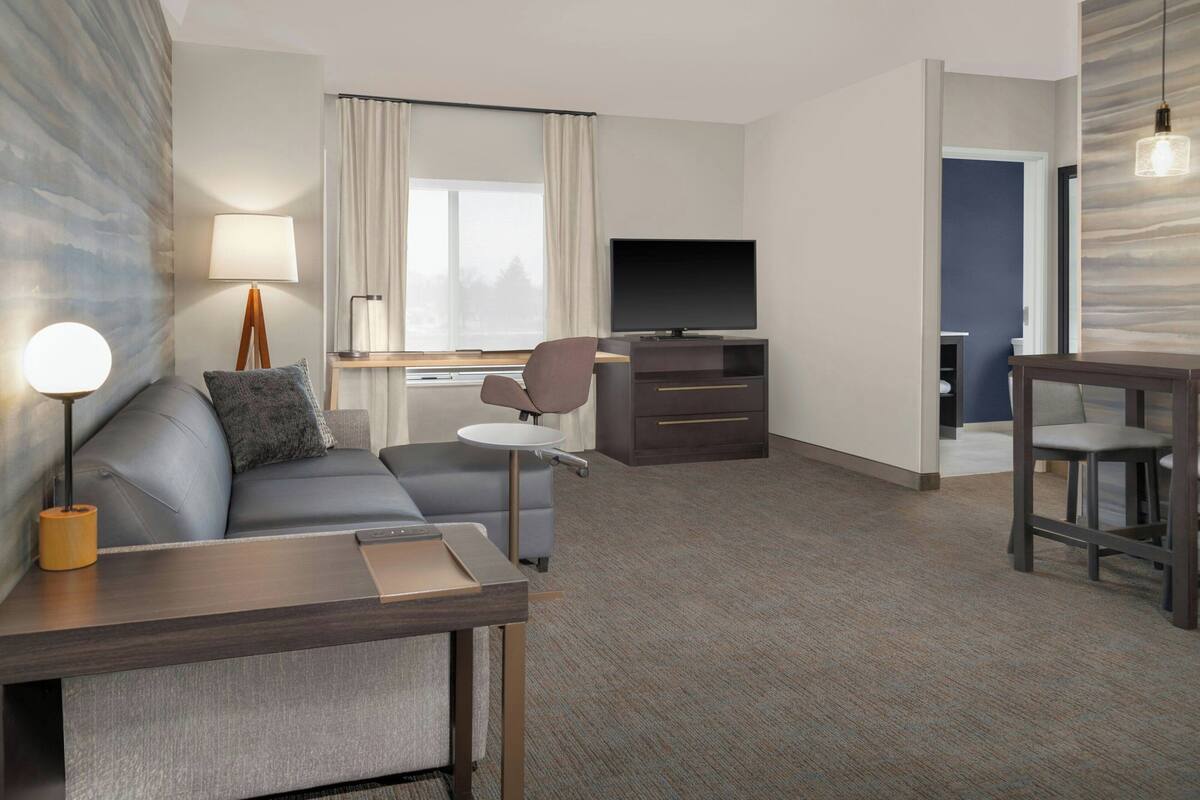 Une chambre d’hôtel moderne équipée d’un canapé, d’une petite table, d’une télévision et d’un bureau.