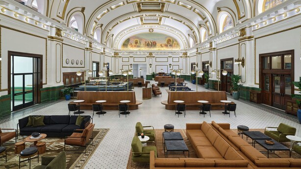 Un hall espacioso con techo alto, detalles arquitectónicos ornamentales y una zona de estar central con sofás y mesas.