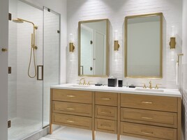 Un baño moderno con cabina de ducha a ras de suelo, dos espejos grandes y un mueble de tocador con varios cajones.
