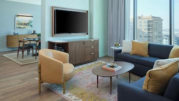 Een moderne woonkamer met een bank, fauteuil, salontafel en een flatscreen televisie aan de muur.