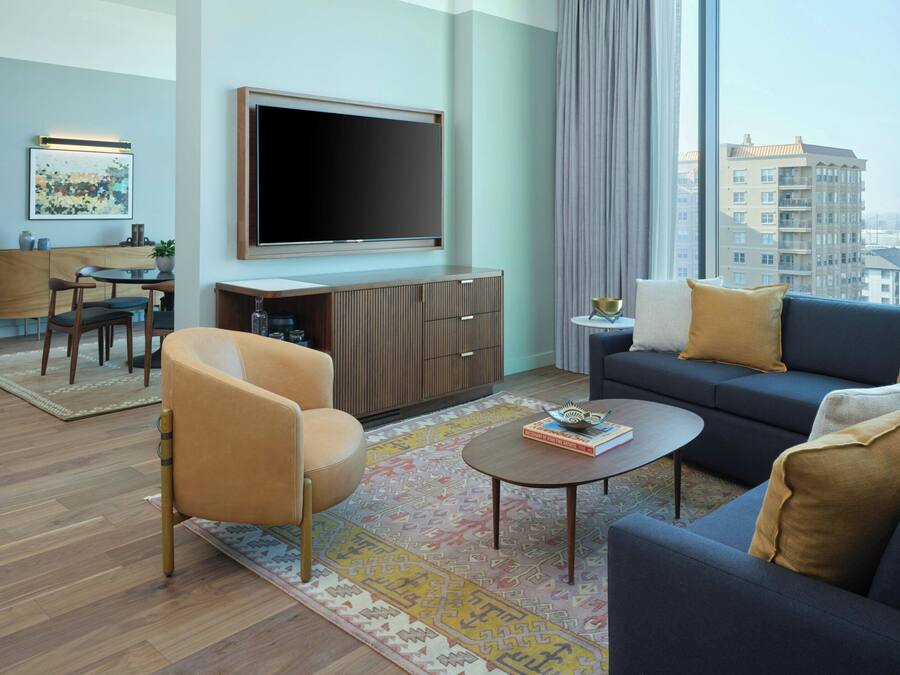 Een moderne woonkamer met een bank, fauteuil, salontafel en een flatscreen televisie aan de muur.