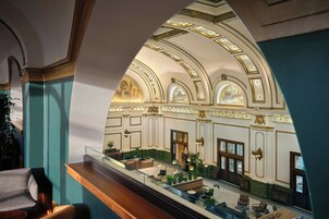 Un vaste hall d’entrée avec un plafond haut, des moulures décoratives et un espace central aménagé avec des tables et des chaises.
