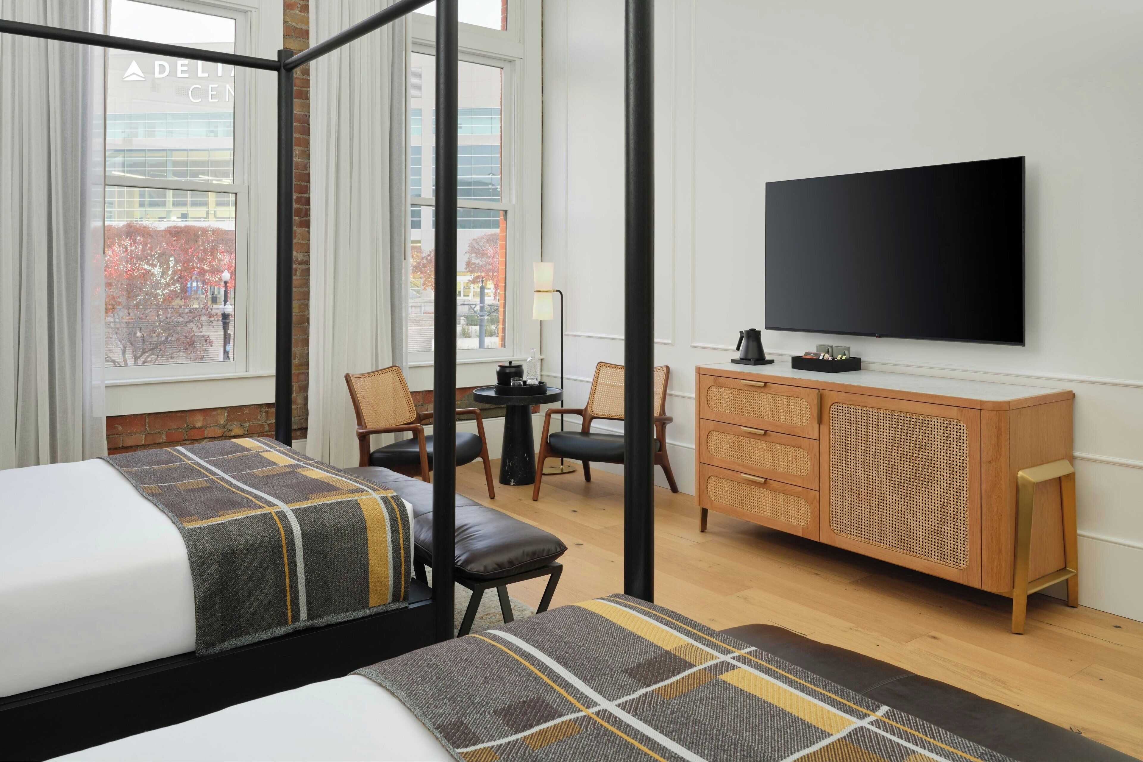 Habitación de hotel con dos camas, televisor, escritorio y vista a un edificio.
