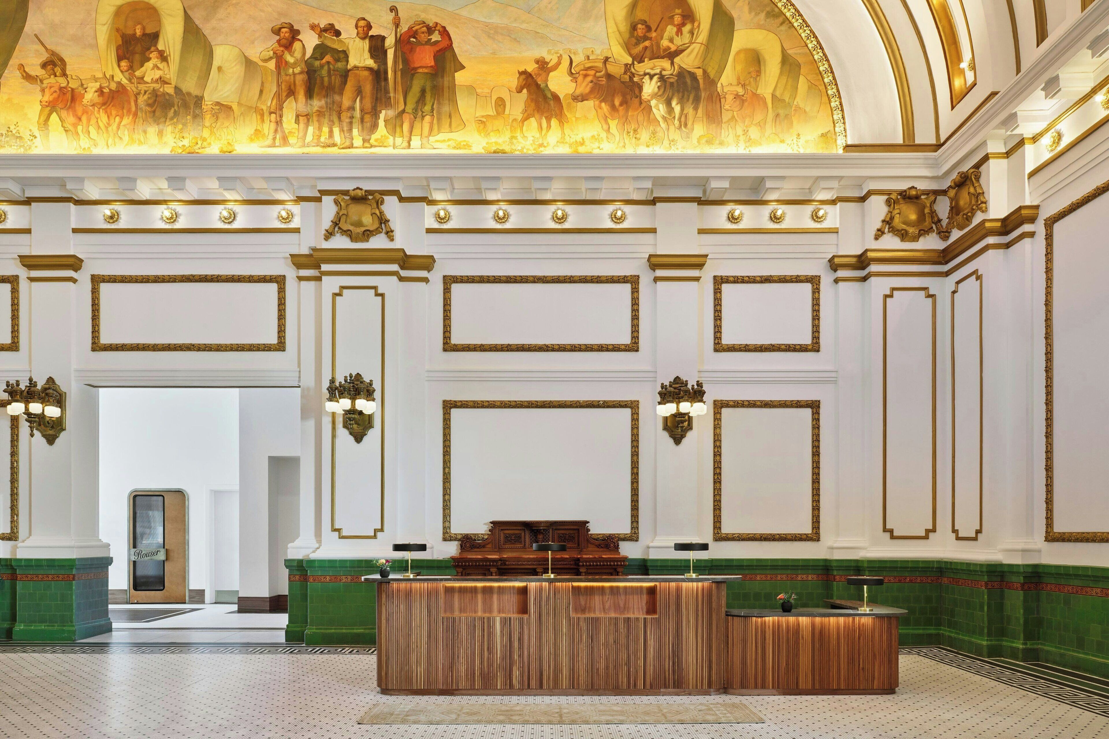 A grand lobby with a wooden reception desk, ornate wall decorations, and a large mural on the ceiling.