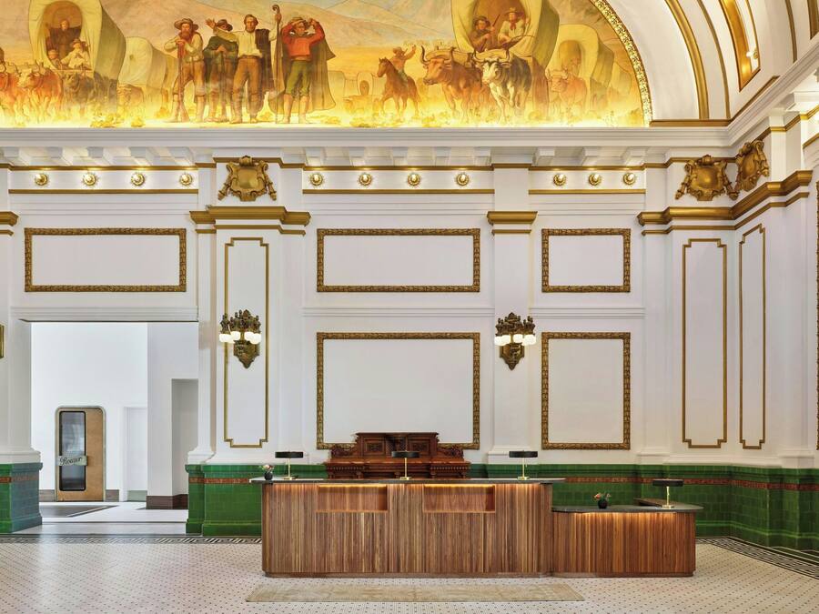 A grand lobby with a wooden reception desk, ornate wall decorations, and a large mural on the ceiling.