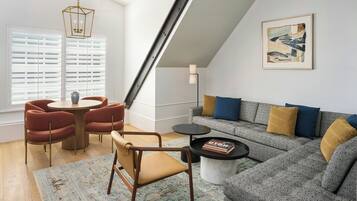A modern living room with a loft-style ceiling, a gray sofa with blue and mustard cushions, a round coffee table, and a dining area with red chairs and a wooden table.