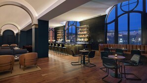 Zona de bar moderna con asientos, barra y grandes ventanales con vista a la ciudad.