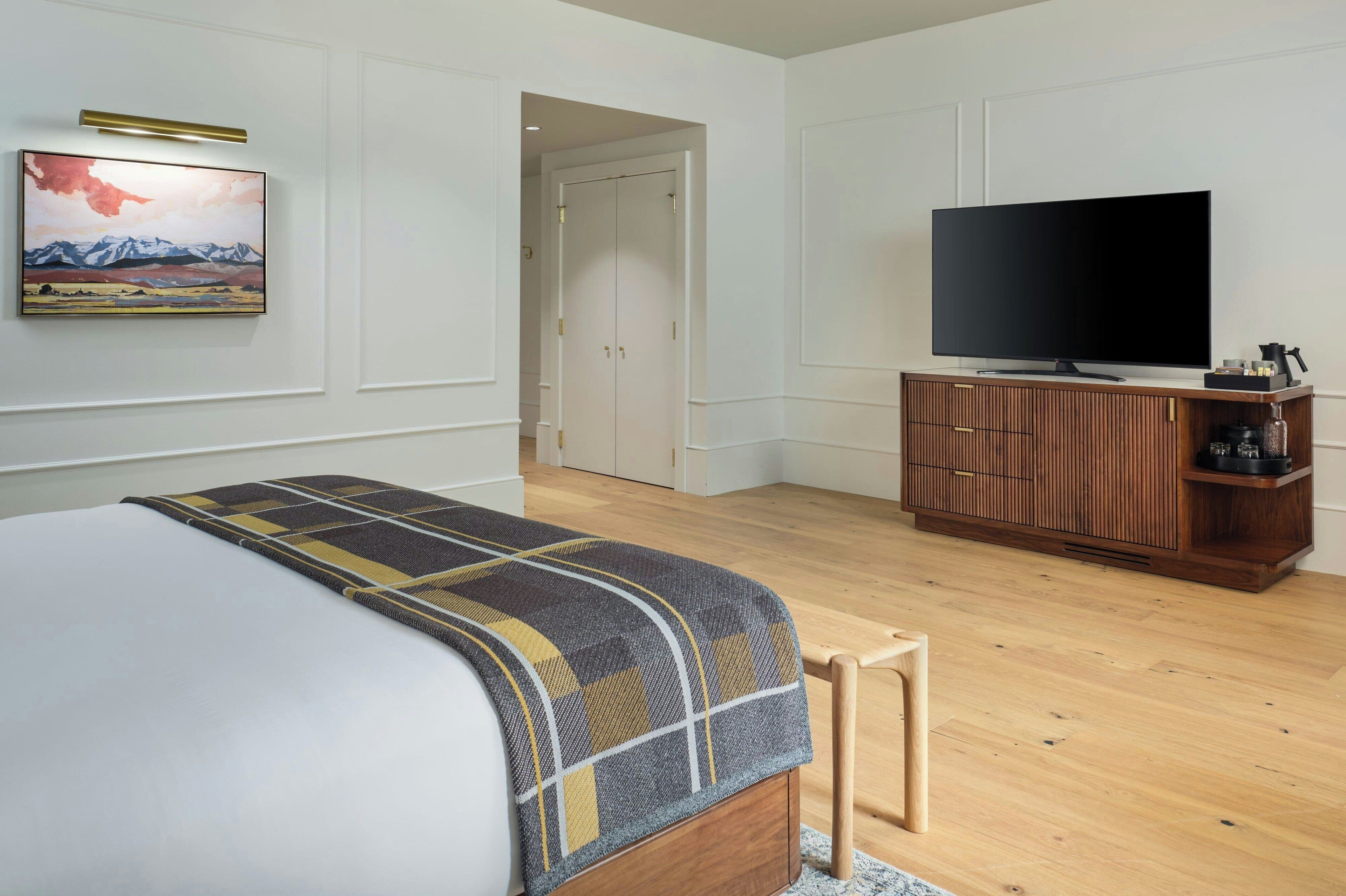 A bedroom with a bed, a television on a wooden cabinet, and a painting on the wall.